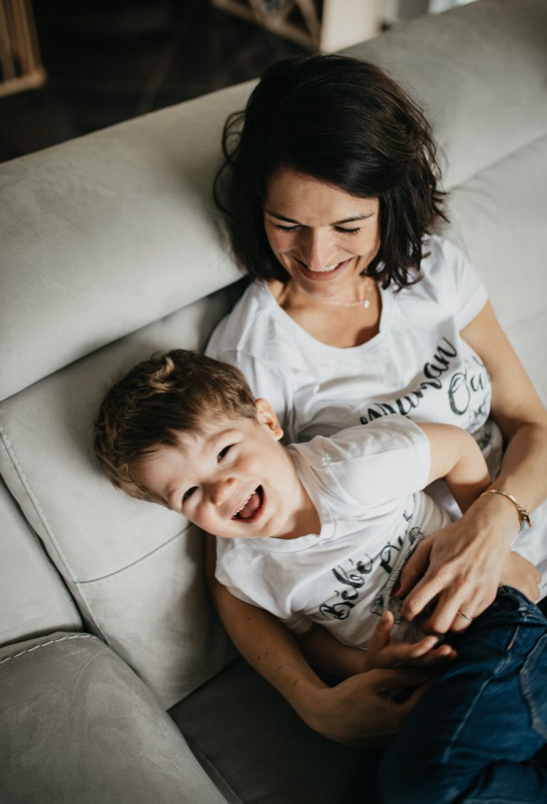 Photo de famille joyeuse prise par Studiow à Mâcon, Villefranche et Beaujolais. La mère et son fils sont complices et se marrent ensemble, capturant parfaitement l'ambiance de la séance photo. Cette image reflète la chaleur et la complicité entre les membres de la famille, et met en valeur le talent du photographe pour capturer des moments spontanés et naturels."
